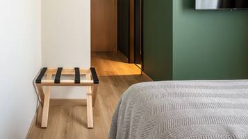 Een hotelkamer met een bed, een klein houten bankje, een televisie aan de muur en een deur naar een andere kamer.