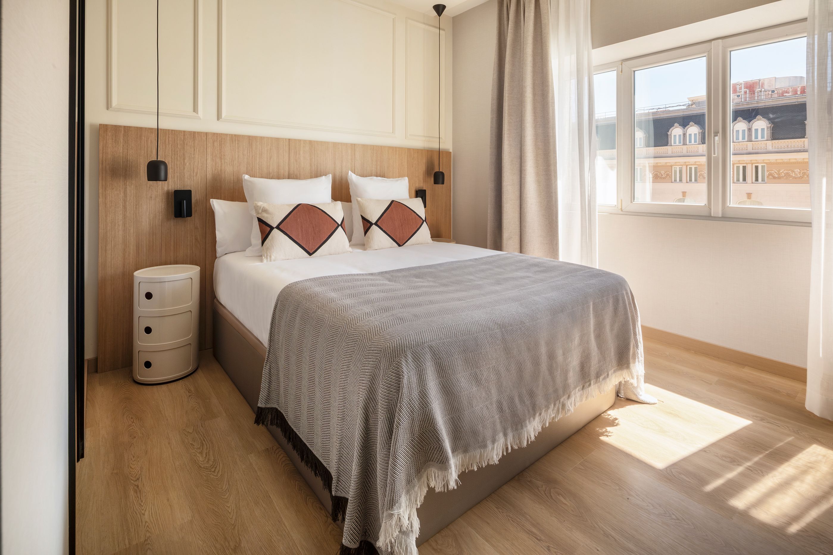 Een opgemaakt bed met een gestreept dekbed, een bedlampje en een nachtkastje met lades.