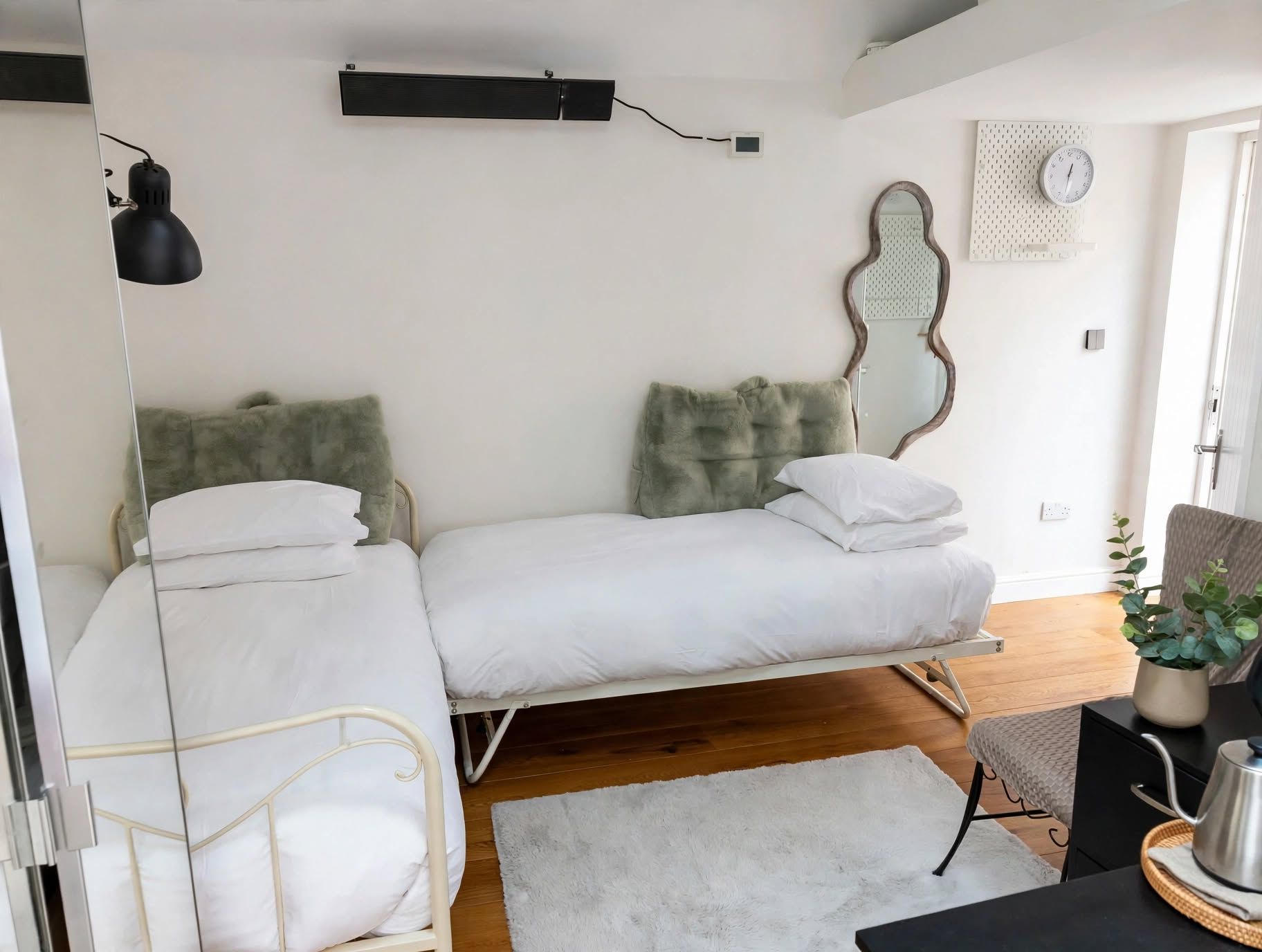 A bedroom with a bed, bedside tables, a mirror, a clock, and a plant.