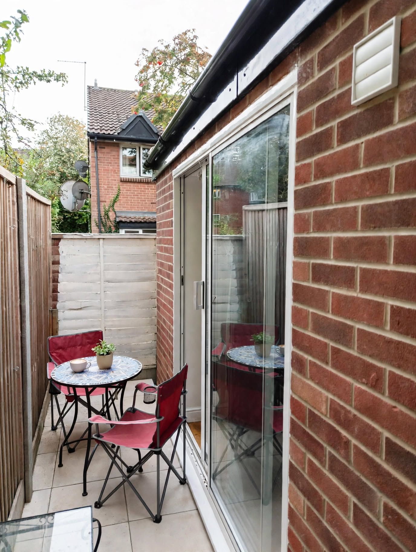 A patio with a table and chairs, a sliding glass door, and a brick wall.