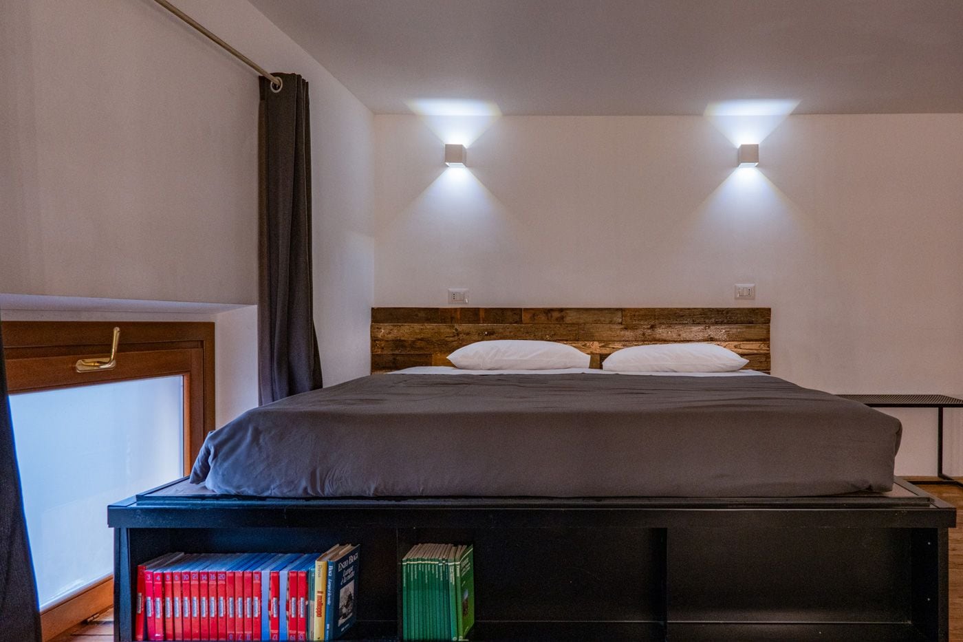 Un lit avec une tête de lit en bois, deux lampes de chevet et une table de chevet avec des livres.