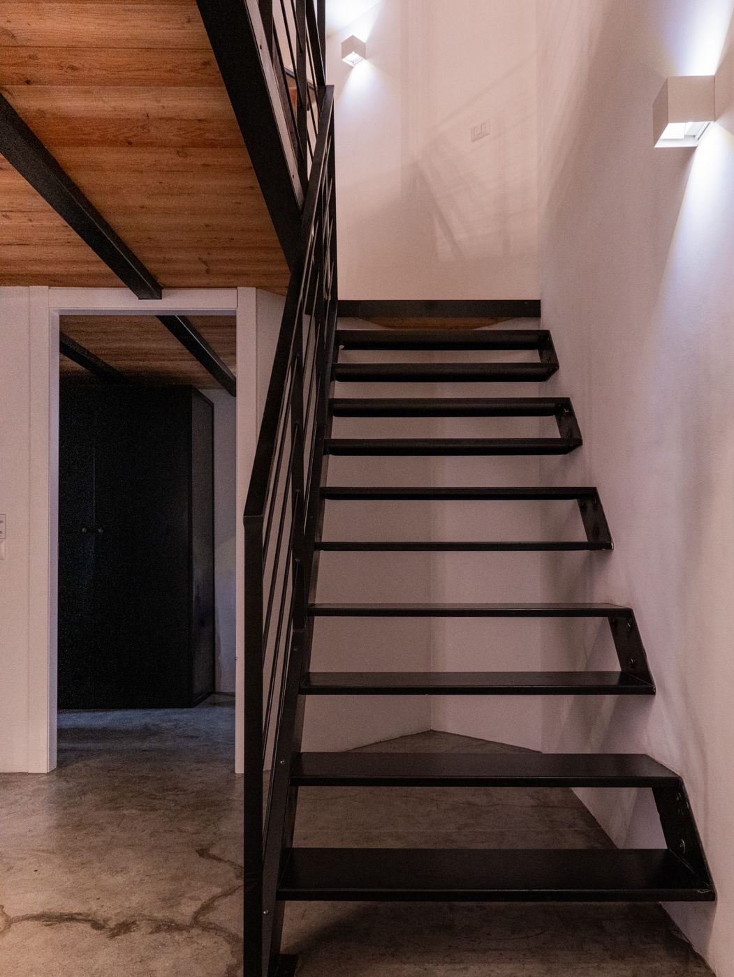 Eine Treppe mit schwarzen Geländern und einer Holzbalkendecke.