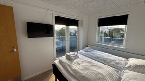 Une chambre à coucher avec un lit, un téléviseur fixé au mur et une fenêtre donnant sur l’extérieur.