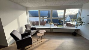 A room with a large window, two armchairs, a small round table, and a potted plant. - Tórshavn Central Guesthouse (Tórshavn)