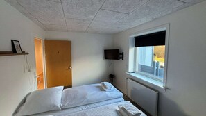 Et værelse med en seng, et fjernsyn på væggen, et vindue og en dør.