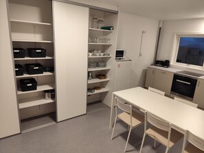 A compact kitchen with white cabinets, a microwave, a stove, and a dining area with a table and chairs. - Tórshavn Central Guesthouse (Tórshavn)