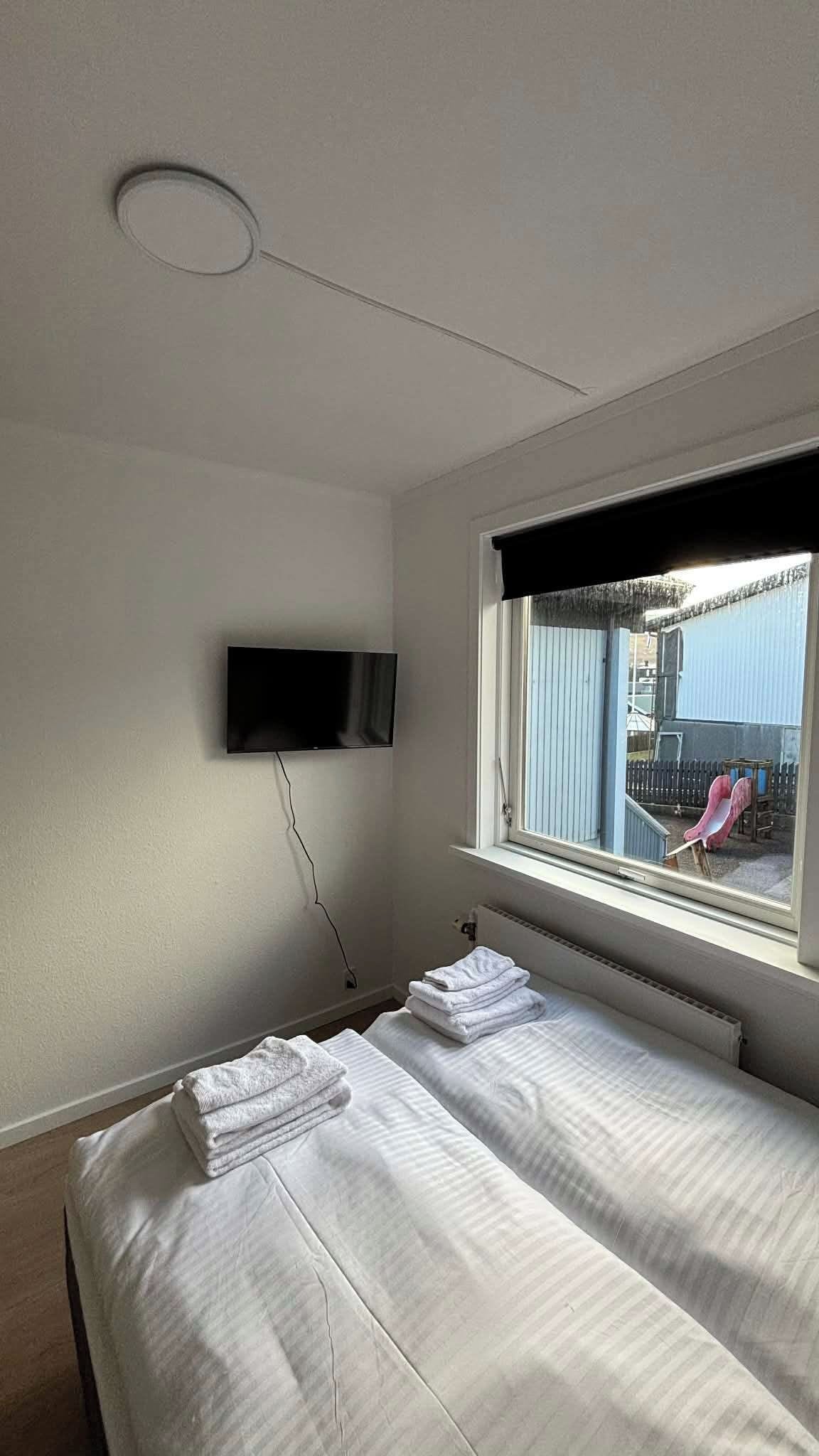 Ein Schlafzimmer mit Bett, einem an der Wand montierten Fernseher und einem Fenster mit Ausblick.