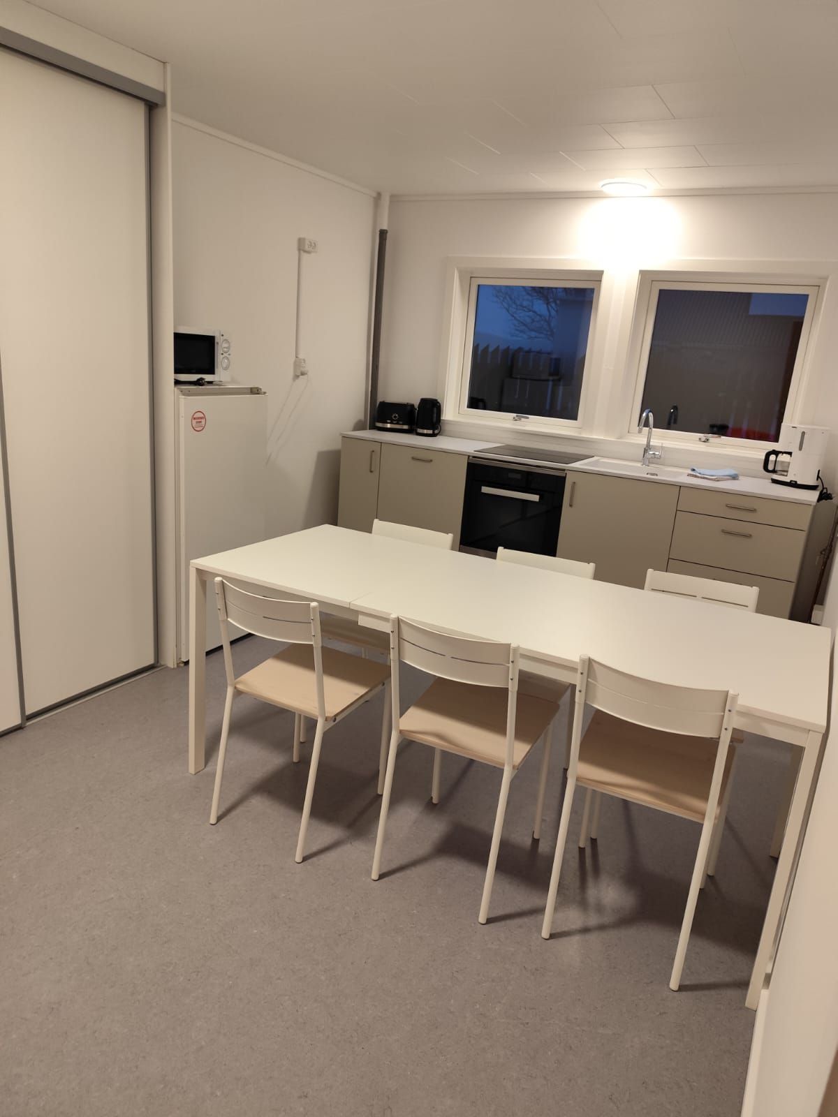 Een kleine keuken met een witte tafel en stoelen, een magnetron en een koffiezetapparaat.