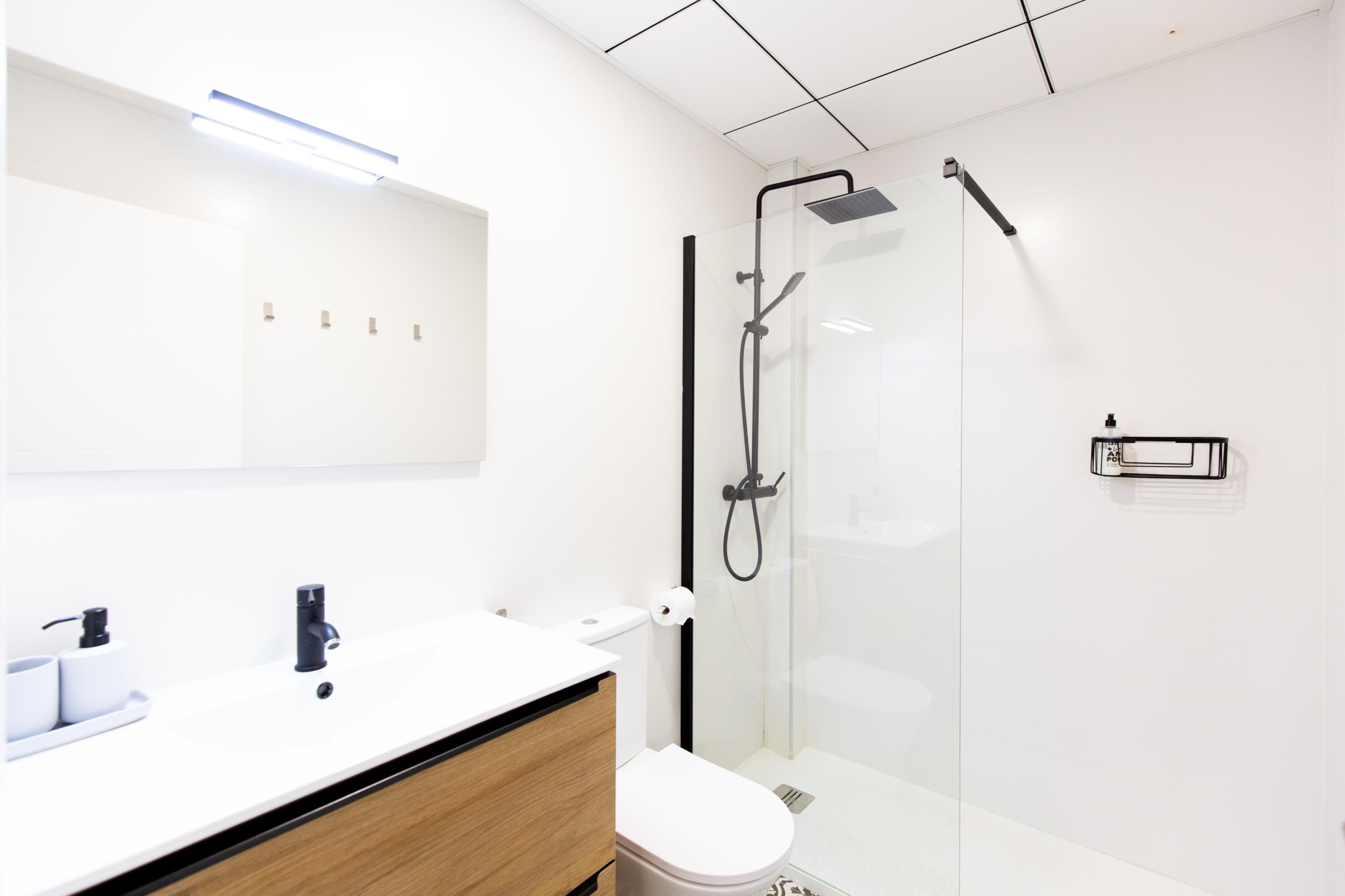 A modern bathroom with a glass shower enclosure, a white sink, and a wooden vanity.