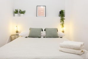 A hotel room with a bed, two bedside lamps, a framed picture on the wall, and two potted plants. - Casa Bitibau   Ground floor apartment close to the Beach (Dénia)
