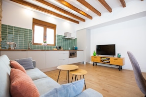Una cocina moderna con ventana, vigas de madera en el techo, horno empotrado y televisor sobre un mueble de madera.