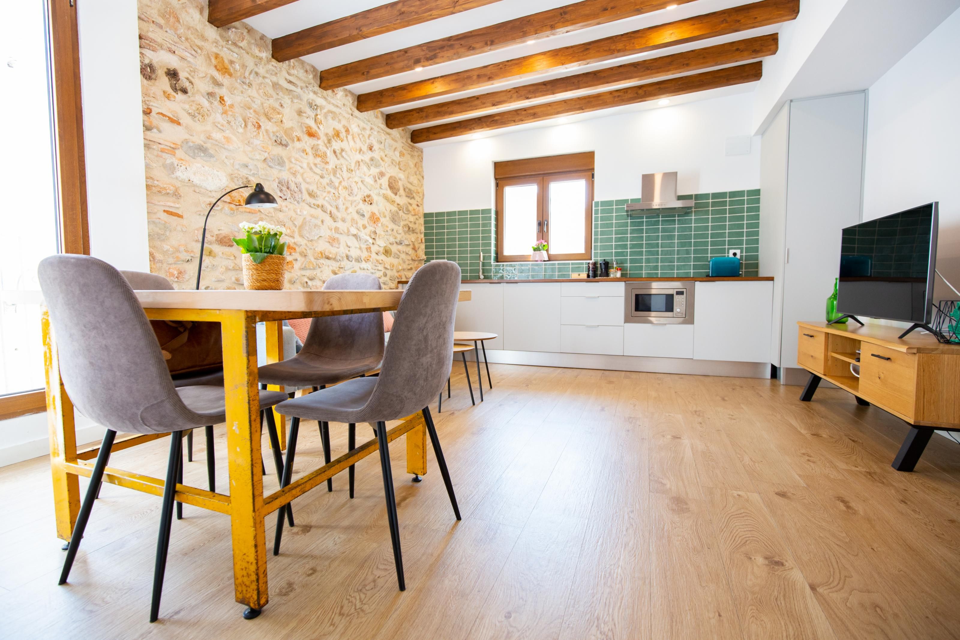 A modern kitchen with a stone wall, wooden beams, and a dining area with a table and chairs.