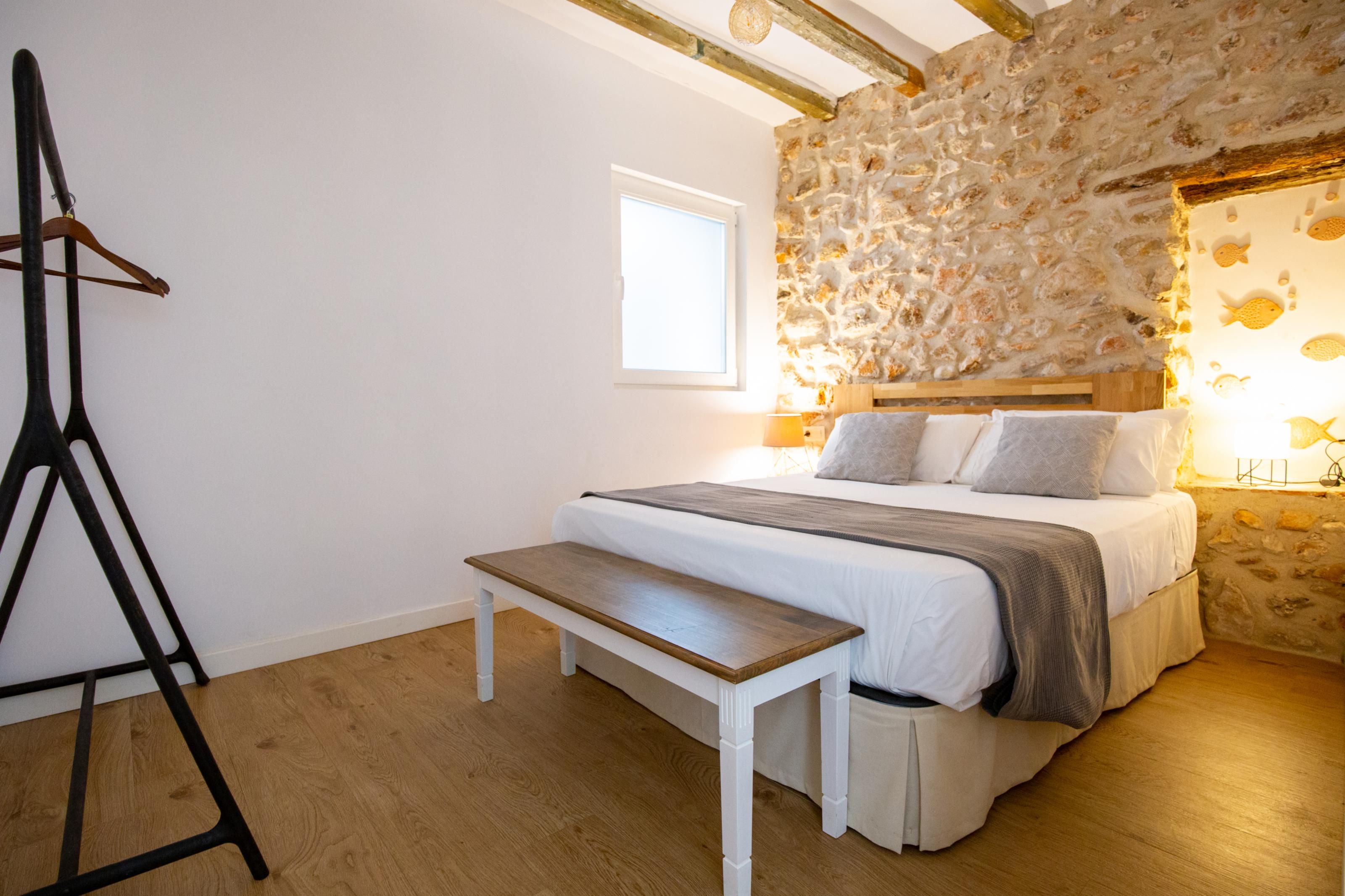 Une chambre avec un mur en pierre, un lit avec de nombreux oreillers, une table de chevet et un banc.