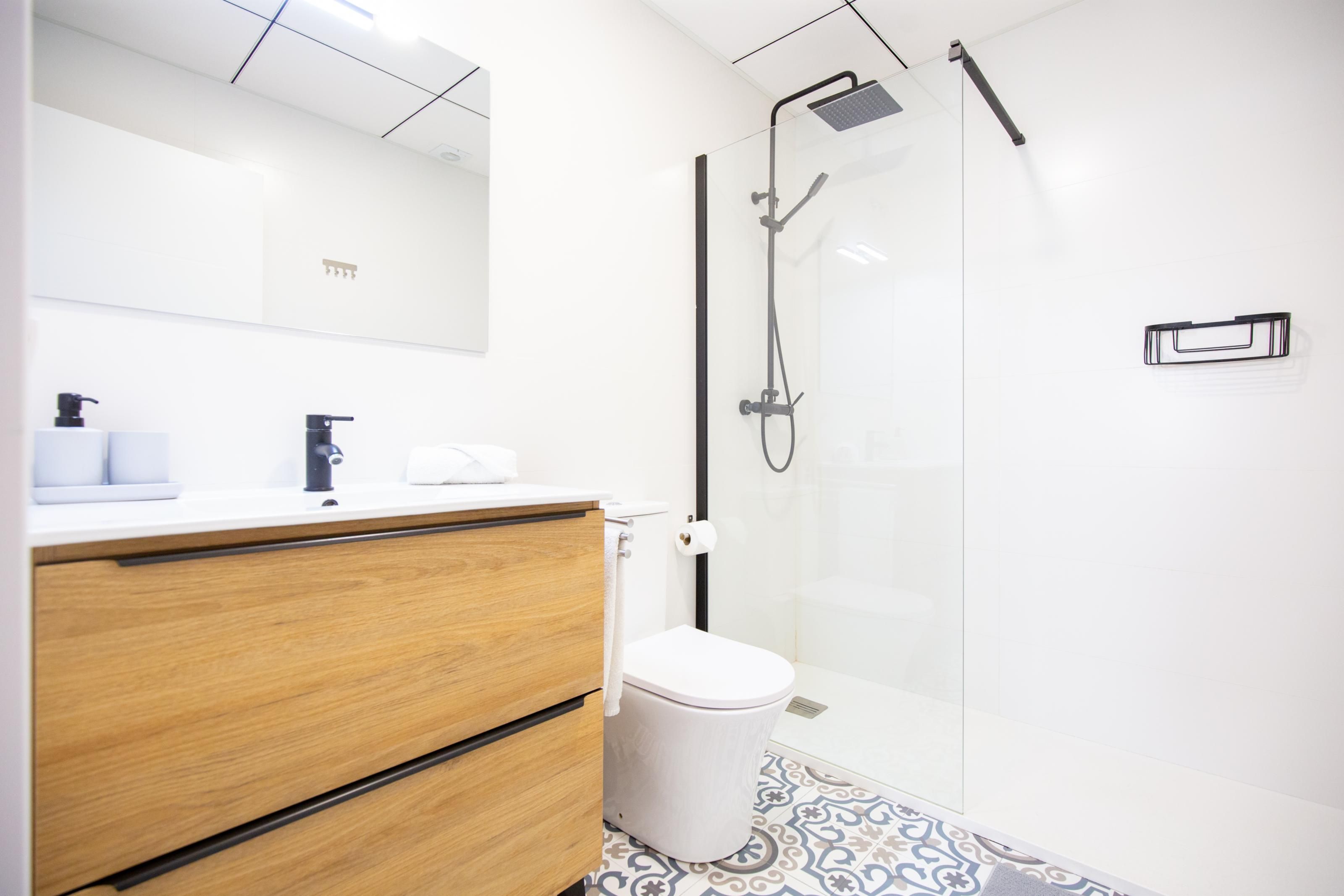 A modern bathroom with a wooden vanity, a toilet, and a glass-enclosed shower area.