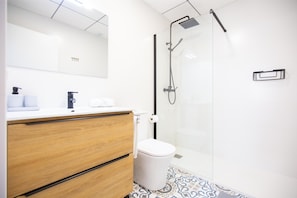 Un baño moderno con tocador de madera, inodoro y zona de ducha con mampara de vidrio.