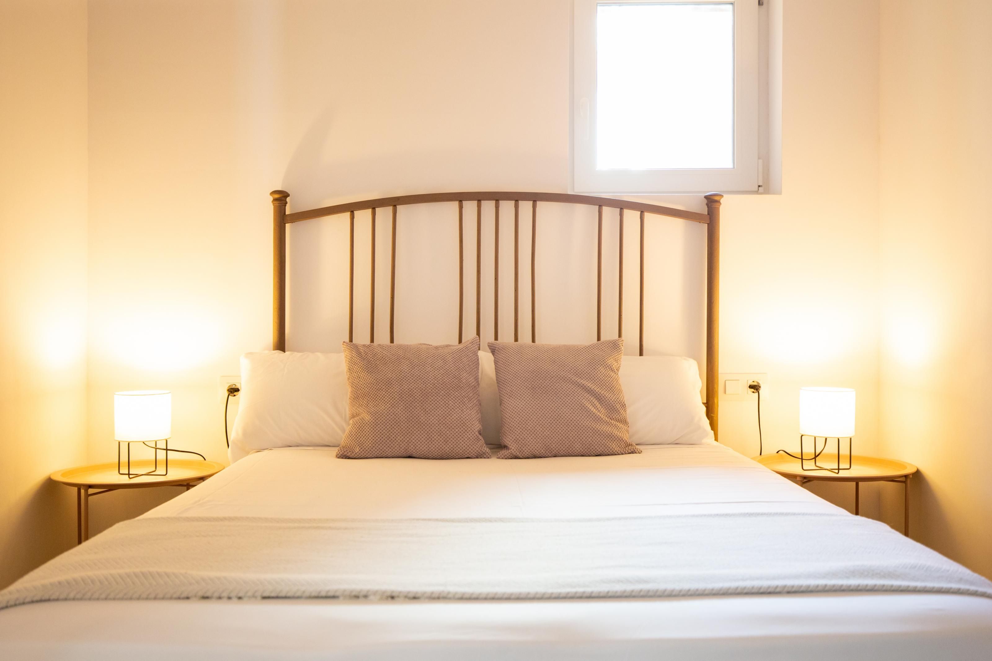 A bed with a headboard, two bedside lamps, and a window above.