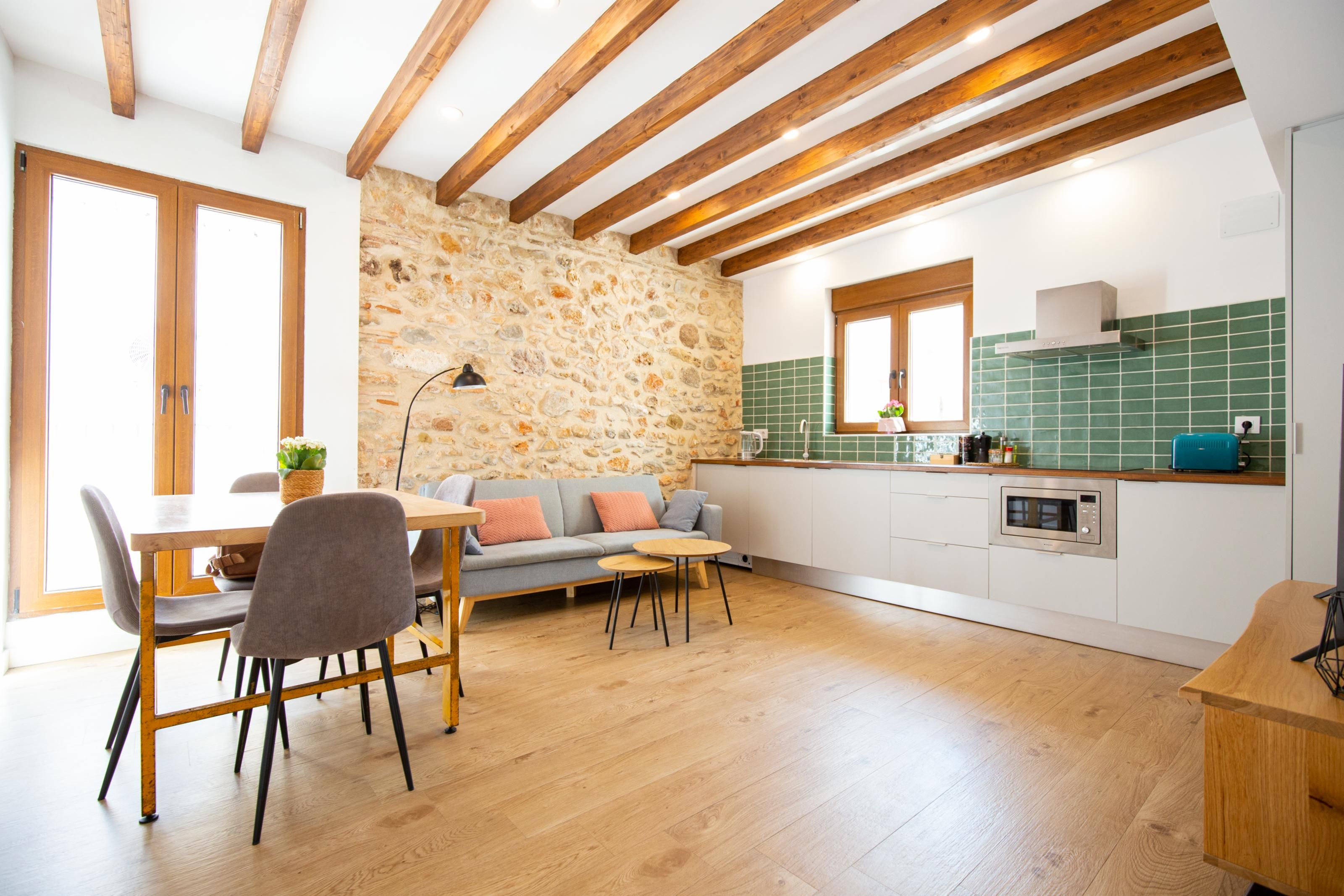 A modern kitchen with a stone wall, wooden beams, and a green tiled backsplash.