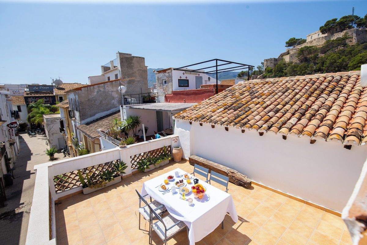 Terraza en la azotea con una mesa lista para comer, con vistas a un paisaje urbano que incluye edificios y una colina.