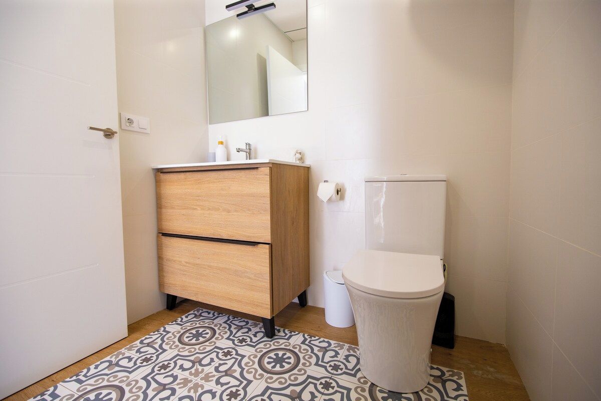 Et badeværelse med et træskab, et toilet og et mønstret gulv.