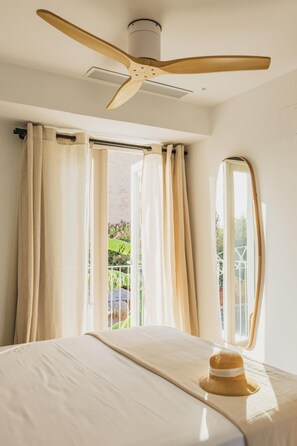 Quarto com cama, ventilador de teto e vista para o verde lá fora.