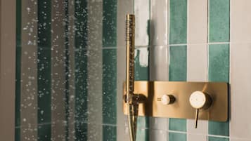 Een douche met een handdouche en een douchekop, beide bevestigd aan een wand met groene tegels.