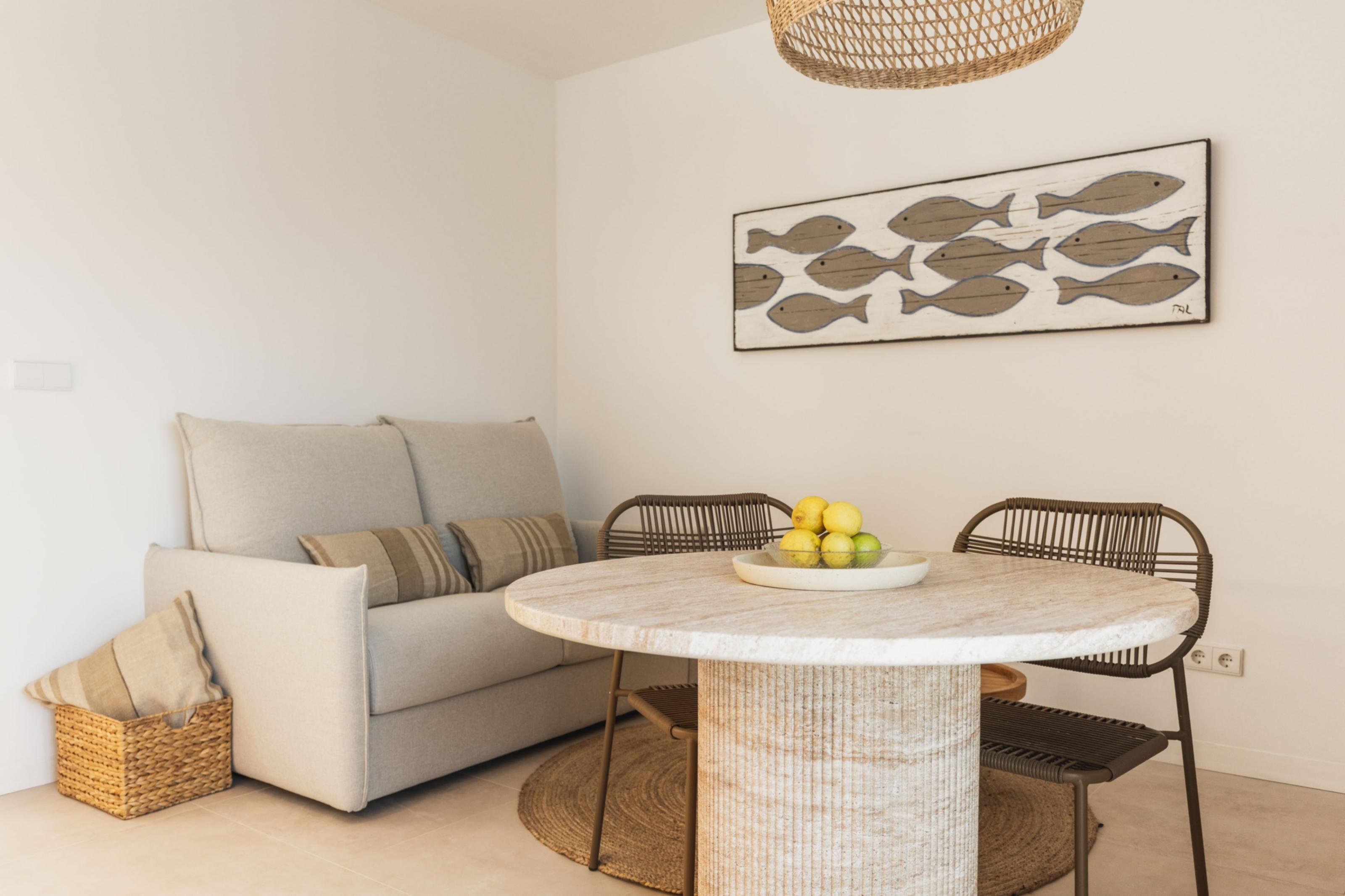 Een minimalistische woonkamer met een ronde tafel, twee stoelen, een bank en een viskunstwerk aan de muur.