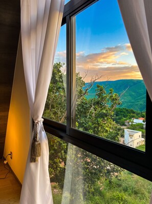 Quarto com uma janela grande com vista para uma paisagem montanhosa.