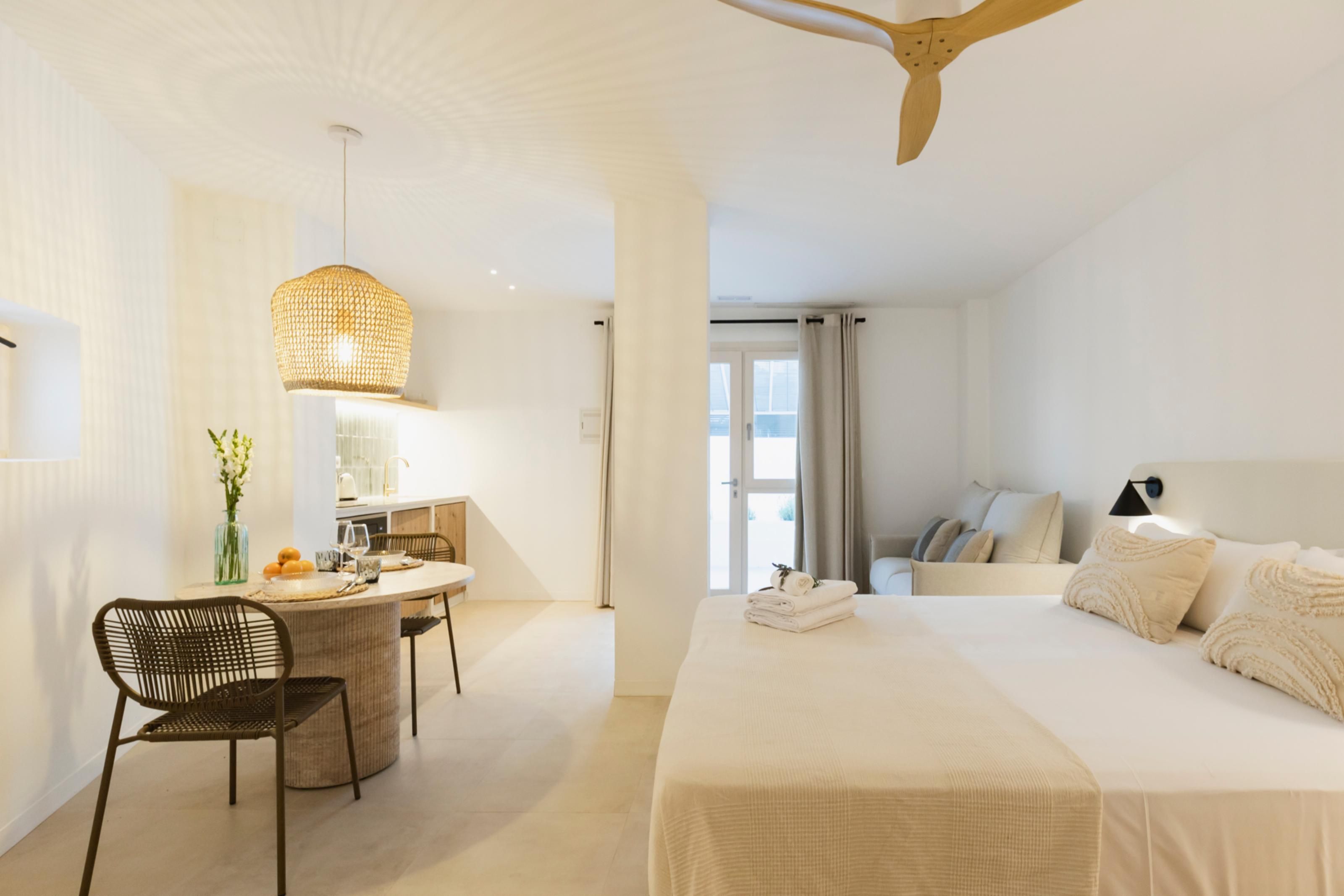 A hotel room with a bed, a desk with a chair, a hanging light fixture, and a view of the outdoors.