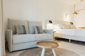 Et moderne soveværelse med en grå sofa, et træsidebord og en seng med hvide sengetøj.