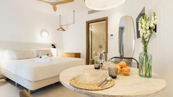 Een moderne hotelkamer met een bed, een ronde eettafel met placemat, een vaas met bloemen en een spiegel aan de muur.