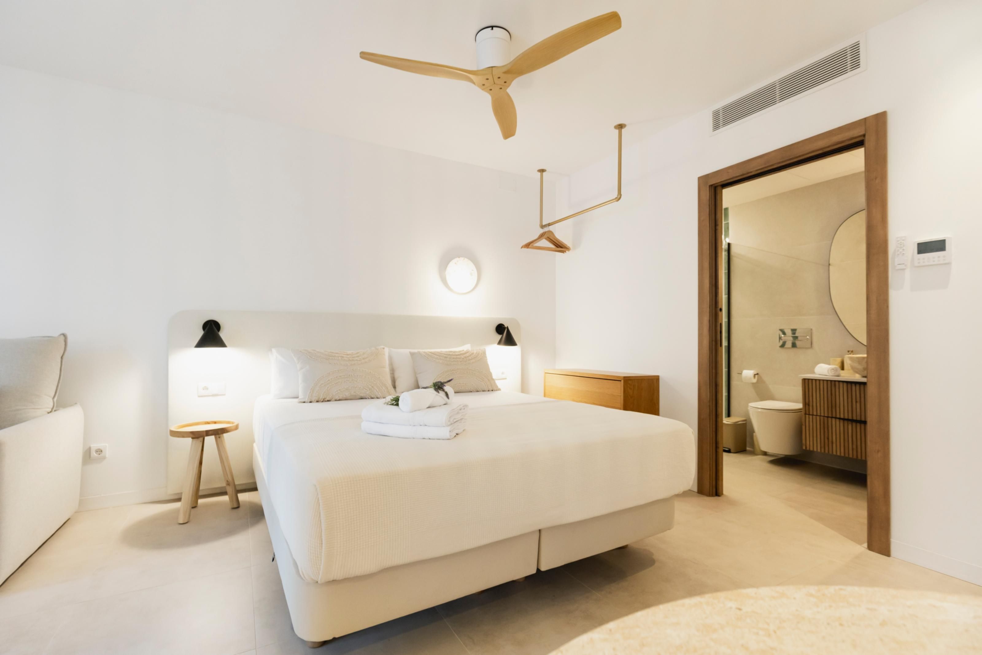 Een moderne slaapkamer met een groot bed, nachtkastjes, een plafondventilator en een badkamer zichtbaar door een geopende deur.