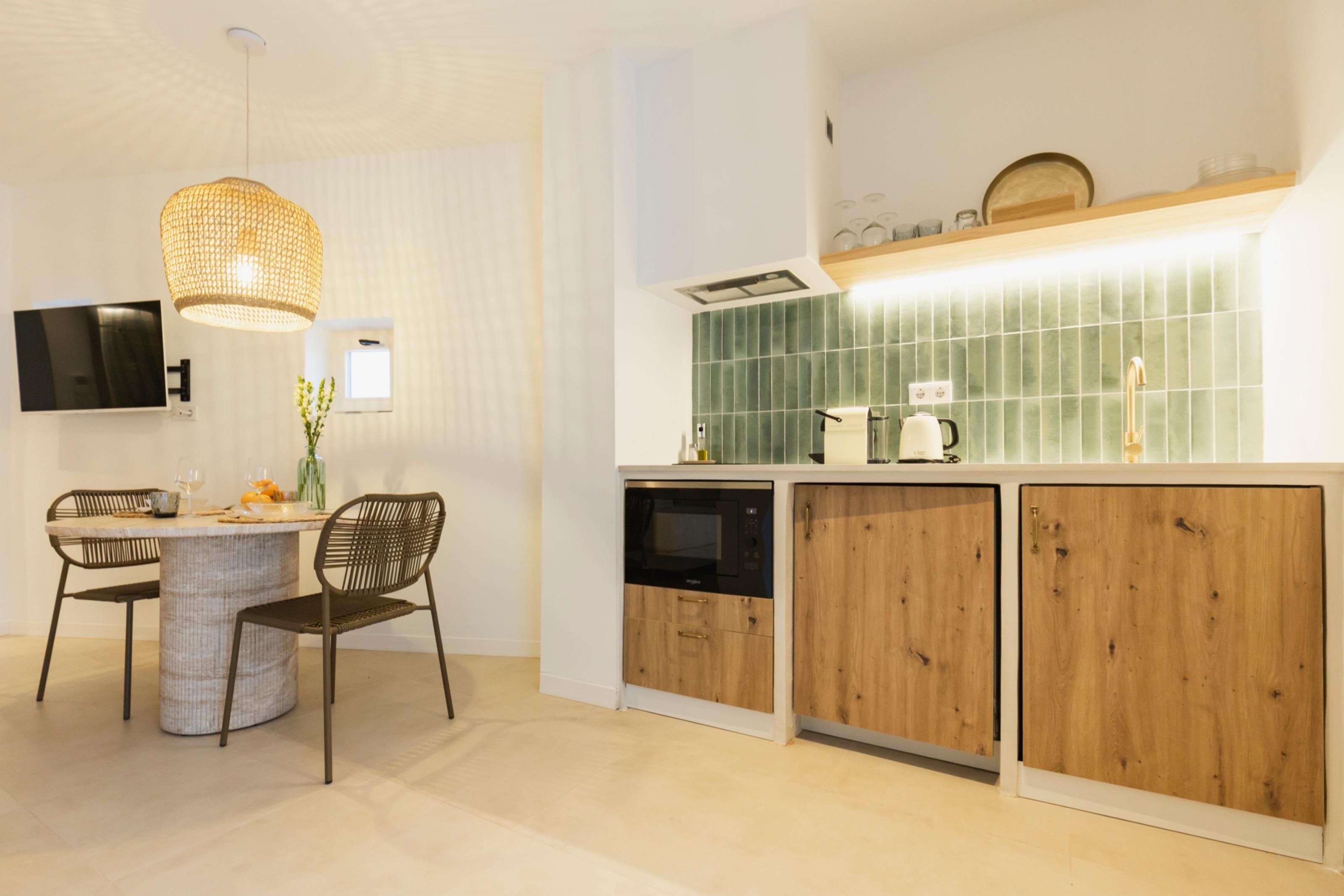 A modern kitchen with a dining area, featuring a round table, two chairs, a hanging light fixture, a built-in oven, and a tiled backsplash.