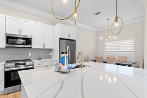 A modern kitchen with white cabinets, stainless steel appliances, a marble countertop, and pendant lighting. - Sleeps 20 • Community Pools • Elegance on the Gulf (Miramar Beach)