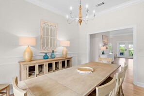 A dining area with a wooden table, chairs, two lamps, a chandelier, and a cabinet with glass doors. - Sleeps 20 • Community Pools • Elegance on the Gulf (Miramar Beach)