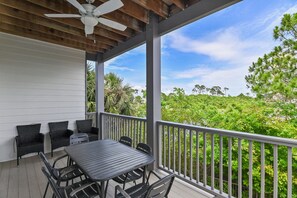 A covered outdoor seating area with a table and chairs, a ceiling fan, and a view of a lush green landscape. - Sleeps 20 • Community Pools • Elegance on the Gulf (Miramar Beach)