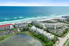 An aerial view of a coastal hotel with multiple buildings, a parking lot, and a beach. - Sleeps 20 • Community Pools • Elegance on the Gulf (Miramar Beach)