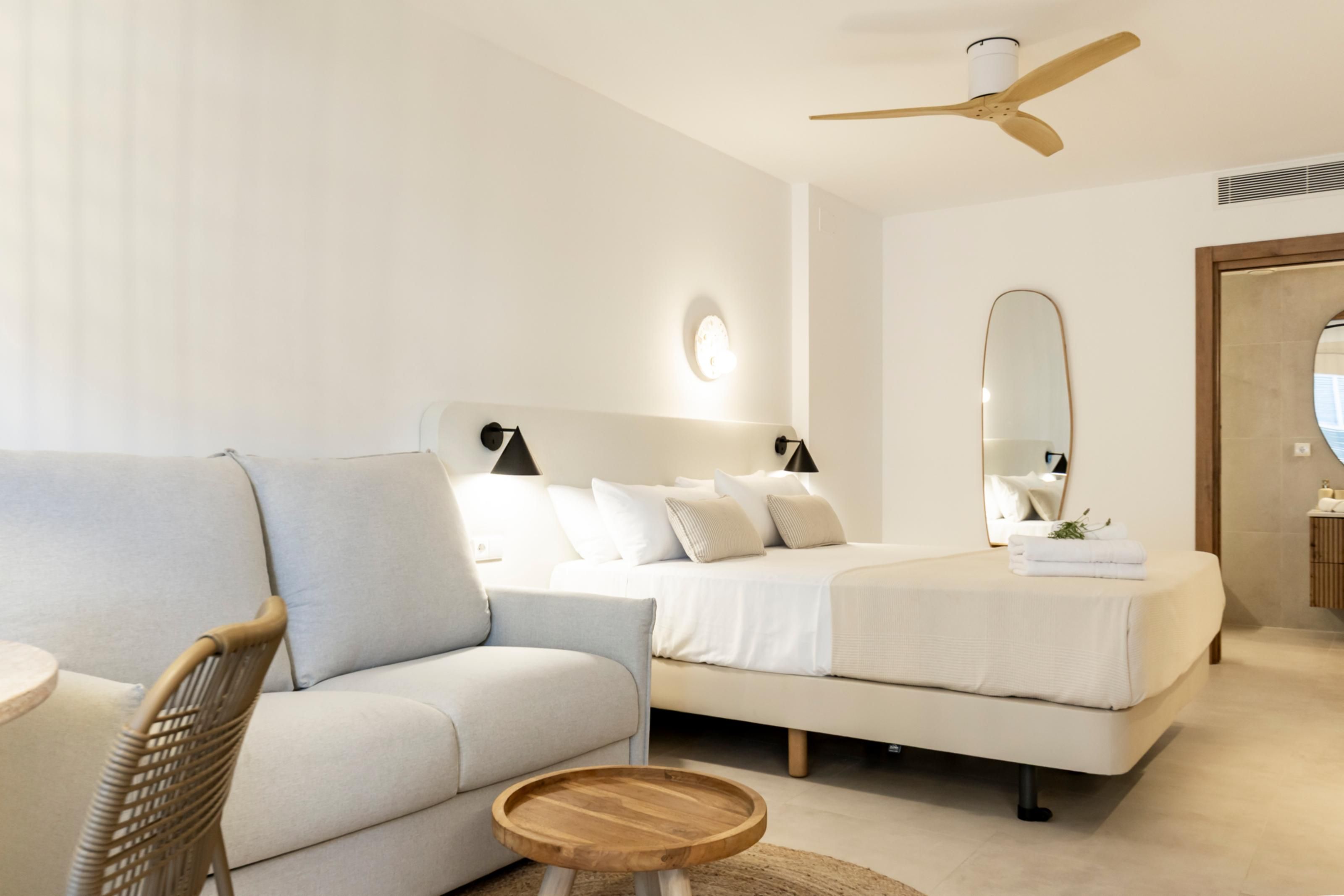 A modern bedroom with a sofa, two beds, a ceiling fan, and a round wooden table.