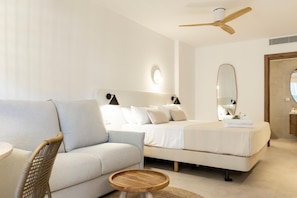 A modern bedroom with a sofa, two beds, a ceiling fan, and a round wooden table. - Vacança Beach: Ground-floor studio with a terrace (Denia)