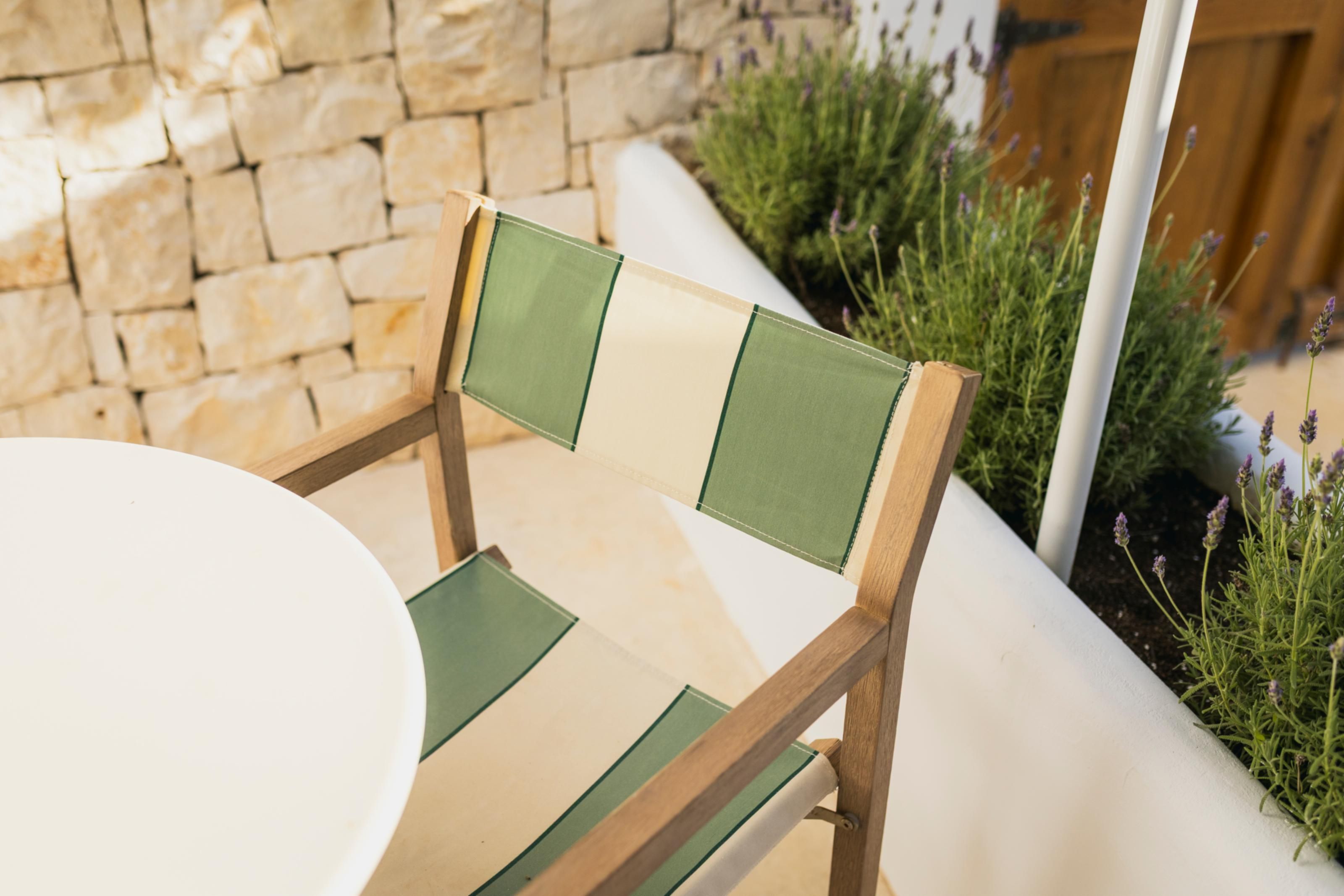 Una silla de madera con respaldo y asiento verde y beige, colocada junto a una mesa blanca.