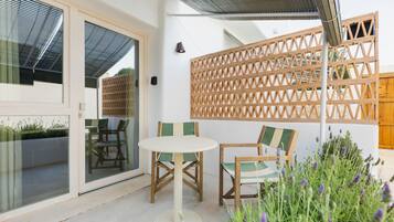 Een terras met een tafel en stoelen, een houten schutting en uitzicht door een glazen deur.