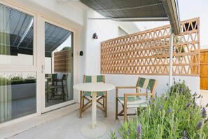 Um pátio com mesa e cadeiras, cerca de madeira e vista através de uma porta de vidro.