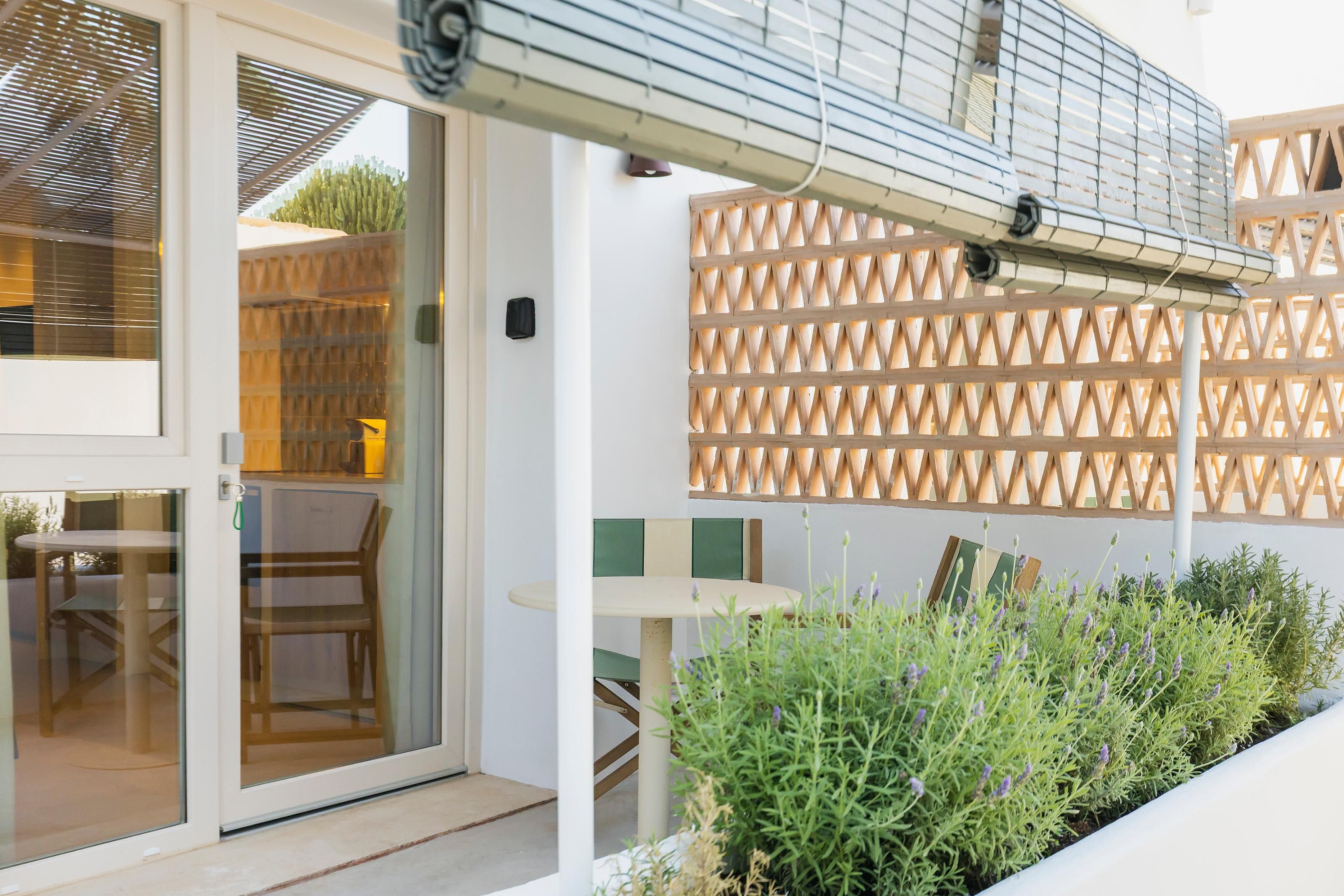 Un área de estar moderna al aire libre, con puerta de vidrio, pared de celosía de madera y una pequeña mesa con sillas.