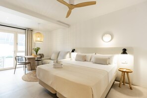 Quarto de hotel moderno com uma cama grande, uma escrivaninha, uma cadeira, uma mesa redonda e um ventilador de teto.
