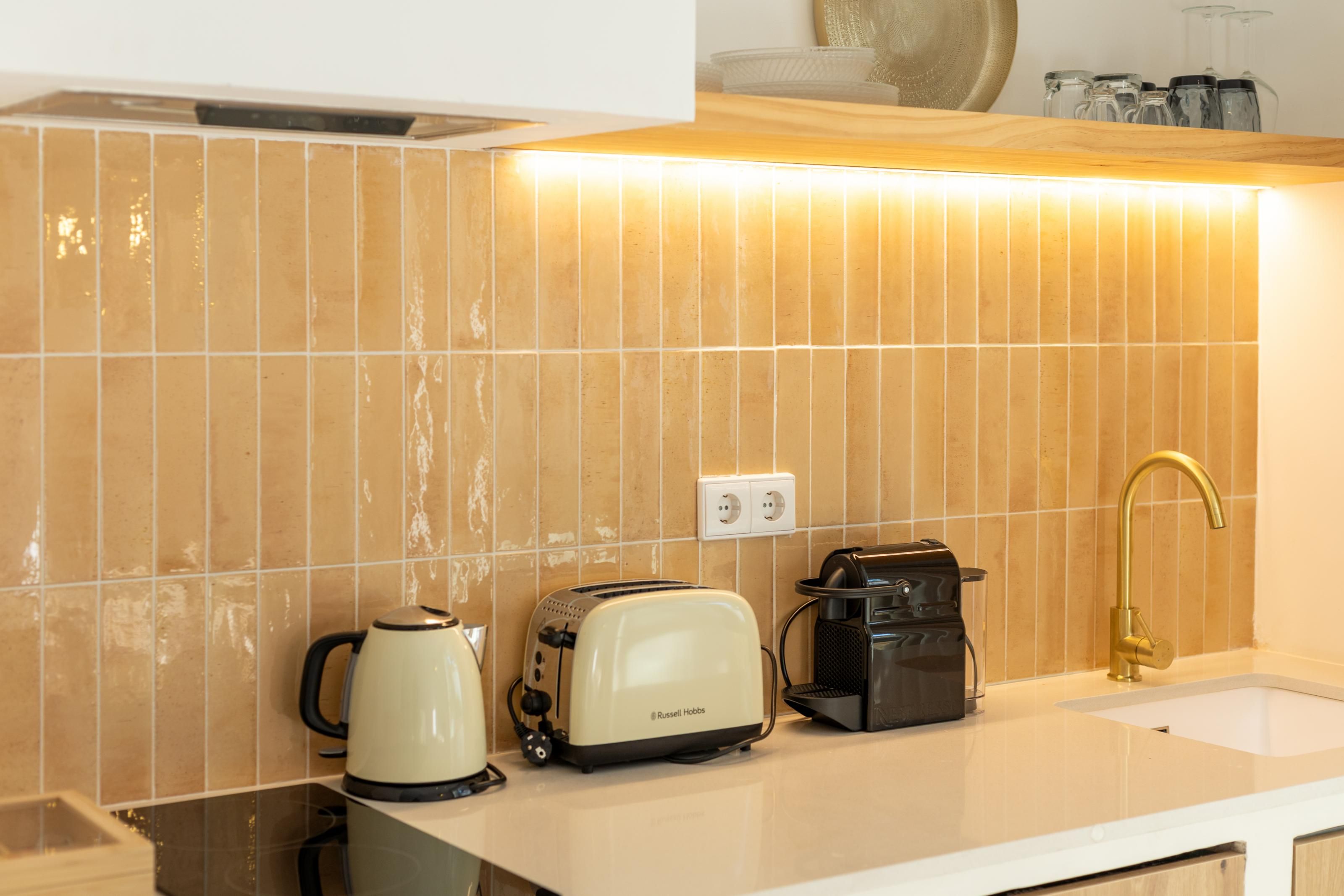 A kitchen with a white countertop, a kettle, a toaster, and a coffee maker.