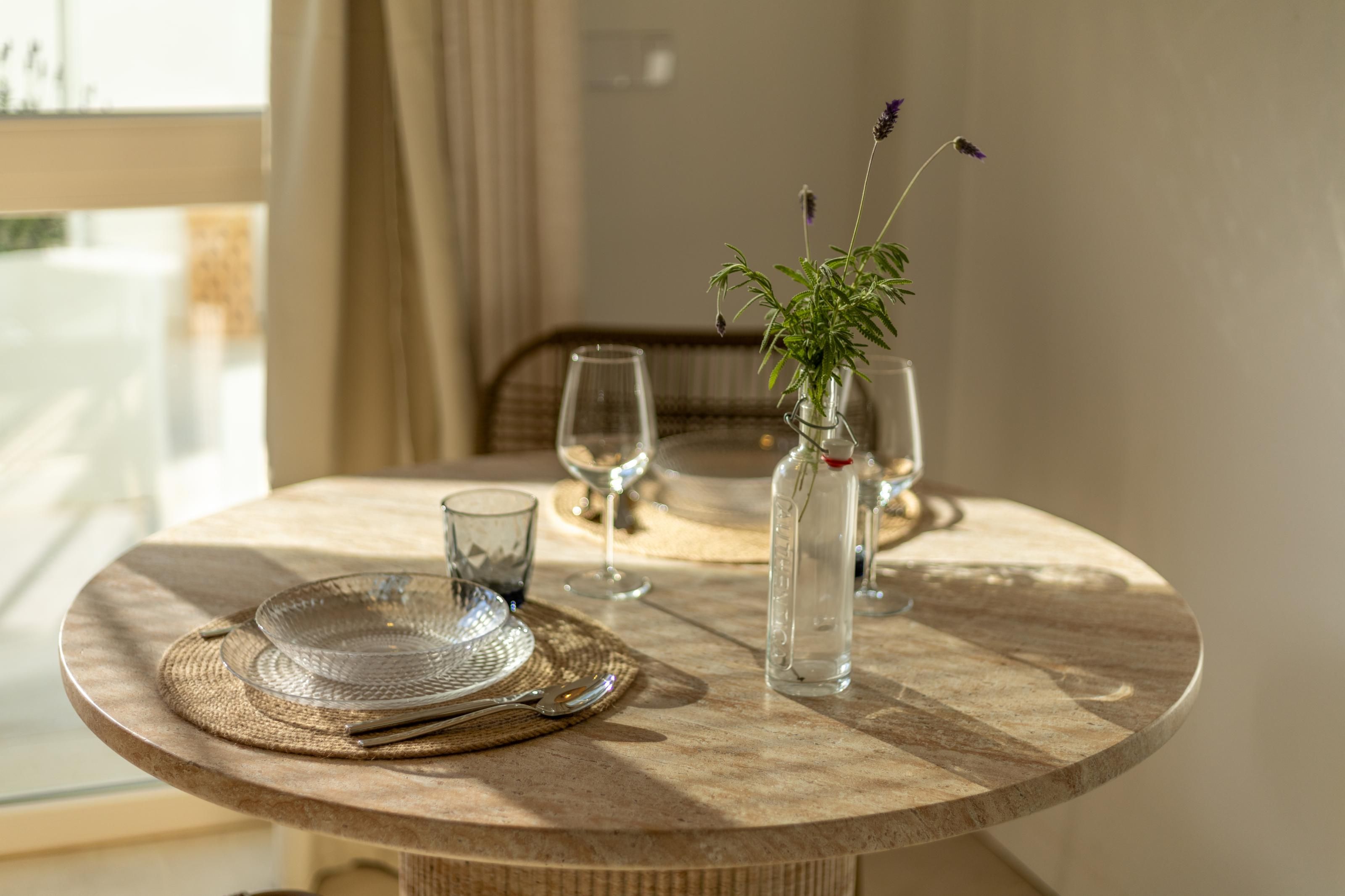 Een ronde eettafel met een glazen vaas met een plant, twee wijnglazen en een helder glazen vaas.