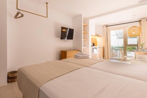 Quarto de hotel com duas camas, televisão, cómoda de madeira, banheiro com chuveiro e varanda com mesa e cadeiras.