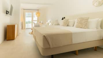 Een hotelkamer met een groot bed, een houten nachtkastje, een bureau met stoel en uitzicht op het groen door een glazen deur.