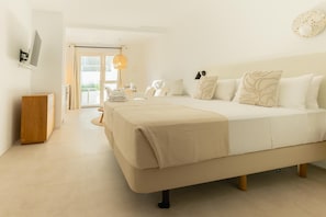 Ett hotellrum med en stor säng, ett litet bord i trä, ett skrivbord med en stol och utsikt över omgivningarna genom en glasdörr.