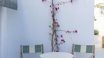 Een klein buitgedeelte met een ronde tafel en twee stoelen, een bloempot met roze bloemen en een witte muur.