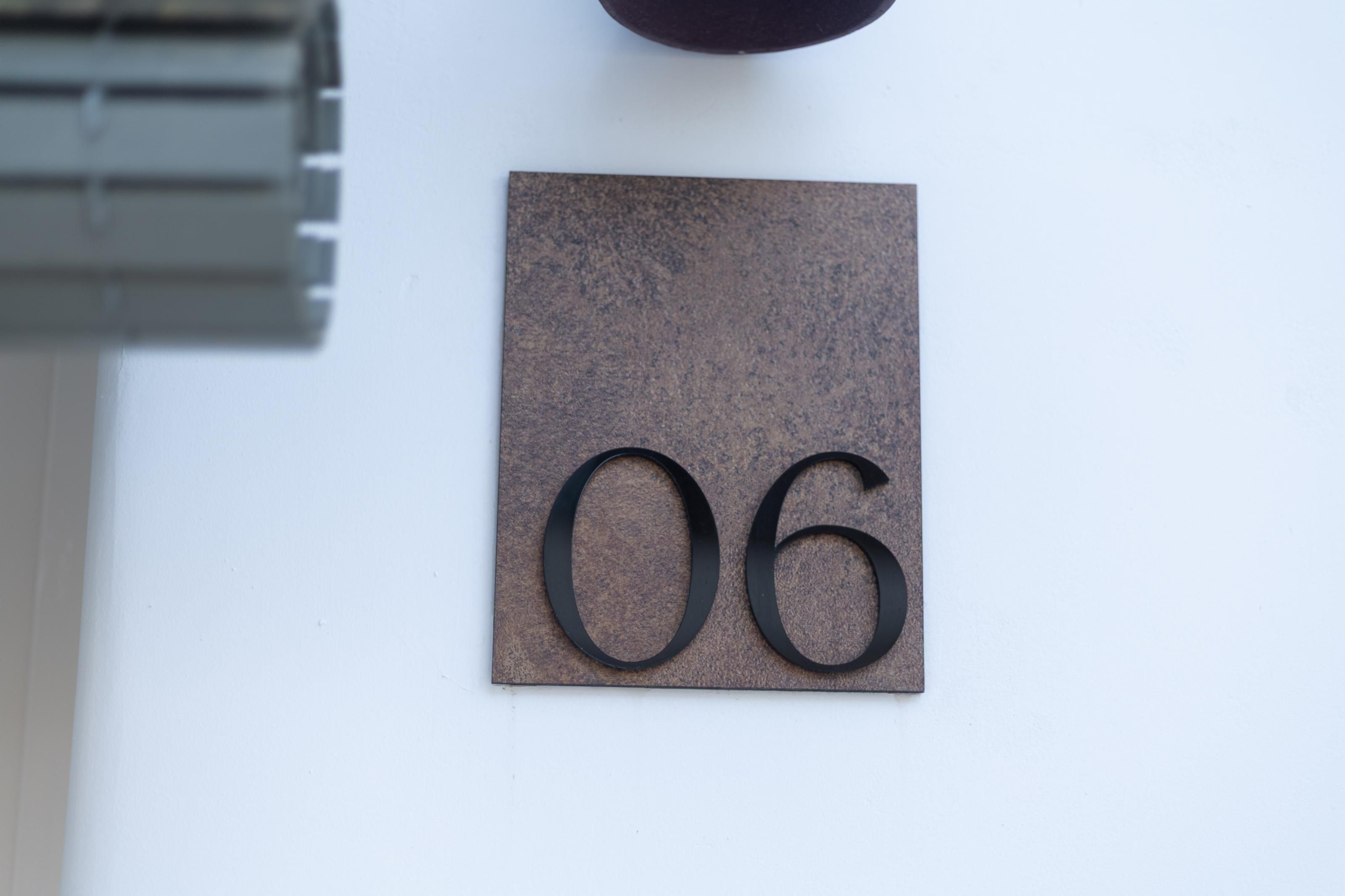 A metallic number plaque with the number 06 affixed to a wall.